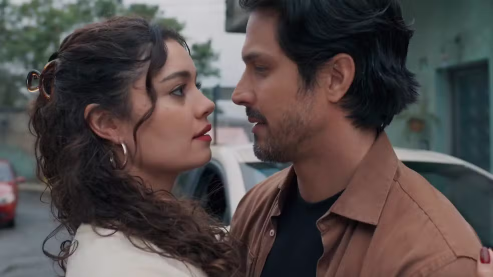 Close do casal Gerluce (Sophie Charlotte) e Paulinho (Rômulo Estrela) olhando-se nos olhos. Ela tem cabelos cacheados presos e brincos de argola; ele tem barba curta e veste uma camisa marrom. Estão em clima de romance antes do casamento na novela Três Graças.