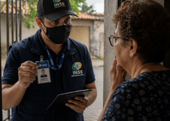 Homem com uniforme e crachá do INSS conversando com idosa na porta de casa