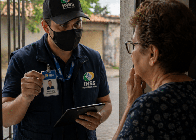 Homem com uniforme e crachá do INSS conversando com idosa na porta de casa