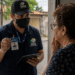 Homem com uniforme e crachá do INSS conversando com idosa na porta de casa