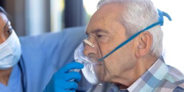 Idoso usando máscara de oxigênio com profissional de saúde ao lado