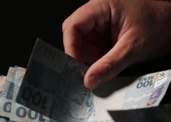 Mão manuseia cédulas de real durante o início dos pagamentos do INSS referentes a julho.