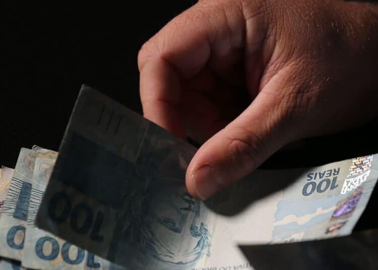 Mão manuseia cédulas de real durante o início dos pagamentos do INSS referentes a julho.