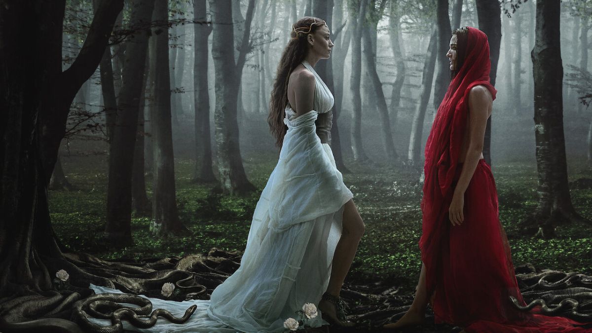 Duas mulheres em trajes medievais em floresta nebulosa com serpentes no chão