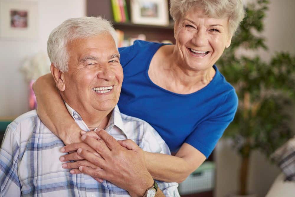 Casal de idosos sorrindo e se abraçando, demonstrando felicidade e os efeitos positivos do riso no bem-estar.