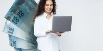 Mulher de cabelos cacheados usando camisa branca segura laptop cinza com notas de 100 reais em leque ao lado