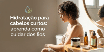 Mulher de costas, cabelos cacheados curtos castanhos, usa toalha bege em frente ao espelho com produtos capilares na bancada