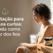 Mulher de costas, cabelos cacheados curtos castanhos, usa toalha bege em frente ao espelho com produtos capilares na bancada
