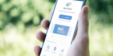 Mão segurando smartphone com app Meu INSS aberto, exibindo botão Entrar com gov.br e ícones de serviços como Revisão do BPC