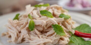 Frango desfiado servido em prato branco com folhas de hortelã