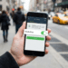 Mão segurando smartphone com app bancário mostrando botão Modo Rua ativado e botão verde Ativar, em rua movimentada com táxis