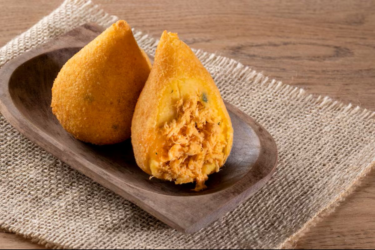 Coxinha aberta recheada com frango desfiado servida em prato de madeira