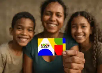 Mãe segura cartão colorido do Programa Bolsa Família ao lado de dois filhos, todos sorrindo