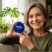 Mulher sorridente de cabelos grisalhos aponta para lata azul de Nivea Creme 150ml em sala com plantas e estante