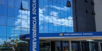 Prédio do INSS com fachada de vidro azul e letreiro "Previdência Social" na entrada, em Brasília