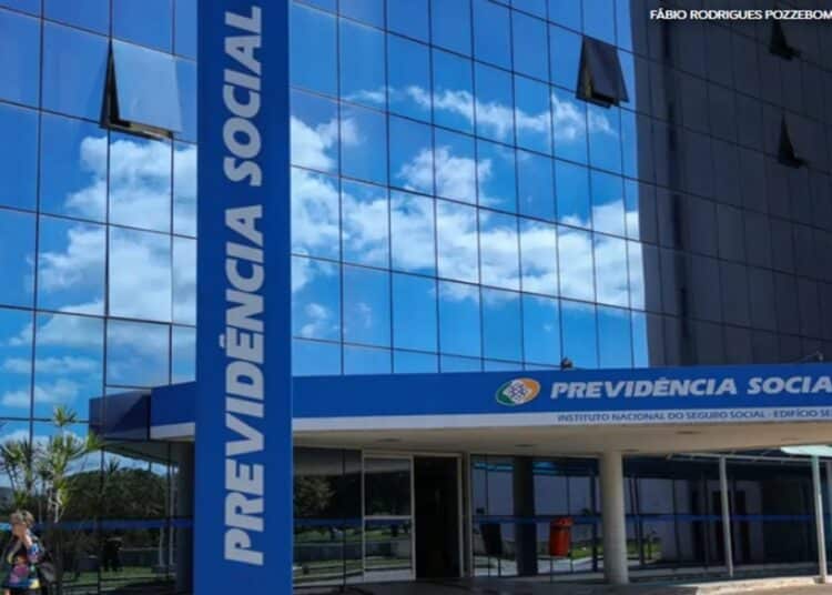 Prédio do INSS com fachada de vidro azul e letreiro "Previdência Social" na entrada, em Brasília