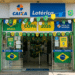 Fachada de lotérica CAIXA com bandeiras do Brasil, bandeirolas e cartazes Copa 2026 nas cores verde e amarela