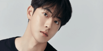 Nam Joo-hyuk, ator coreano de cabelos escuros e camiseta preta, em foto de ensaio com fundo cinza claro