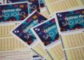 Volantes temáticos da Quina de São João empilhados, exibindo bandeirinhas coloridas e grade numérica para apostas