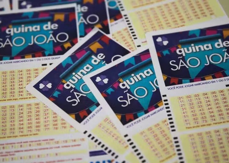 Volantes temáticos da Quina de São João empilhados, exibindo bandeirinhas coloridas e grade numérica para apostas