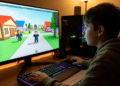 Menino de costas jogando Roblox em computador desktop com teclado mecânico RGB e monitor exibindo avatares coloridos