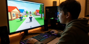 Menino de costas jogando Roblox em computador desktop com teclado mecânico RGB e monitor exibindo avatares coloridos