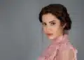 Ece İrtem com cabelo castanho trançado e blusa rosa de renda em fundo cinza, em ensaio fotográfico