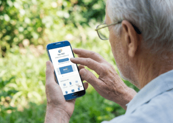 Homem idoso de cabelos brancos e óculos usa smartphone exibindo app Meu INSS em área externa verde