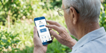 Homem idoso de cabelos brancos e óculos usa smartphone exibindo app Meu INSS em área externa verde
