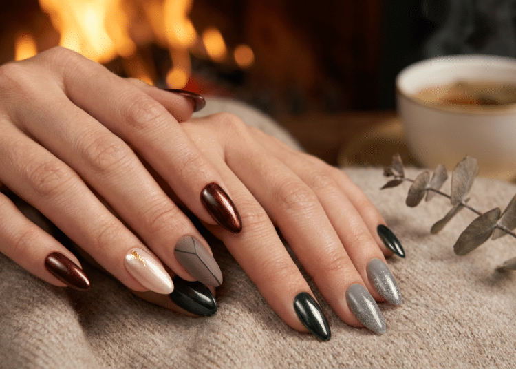 Mãos femininas com unhas amendoadas em esmalte vinho metálico, verde escuro e cinza prateado sobre tecido bege