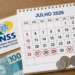 Calendário de julho 2026 com datas marcadas, cartão INSS, dinheiro e moedas ao lado