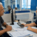 Idoso recebe atendimento de mulher usando calculadora em balcão com papéis e computador