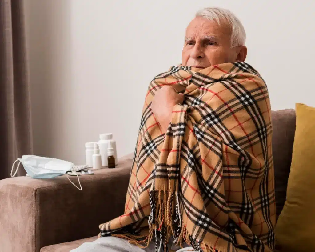 Frio nos idosos Homem idoso envolvido em cobertor para se proteger do frio dentro de casa.