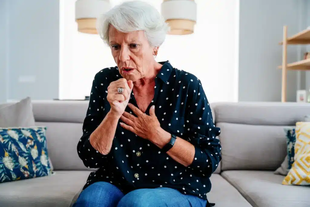 Mulher idosa tossindo e levando a mão ao peito enquanto apresenta desconforto respiratório.