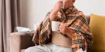 Idoso agasalhado com lenço e caneca apresenta sintomas respiratórios durante o frio.