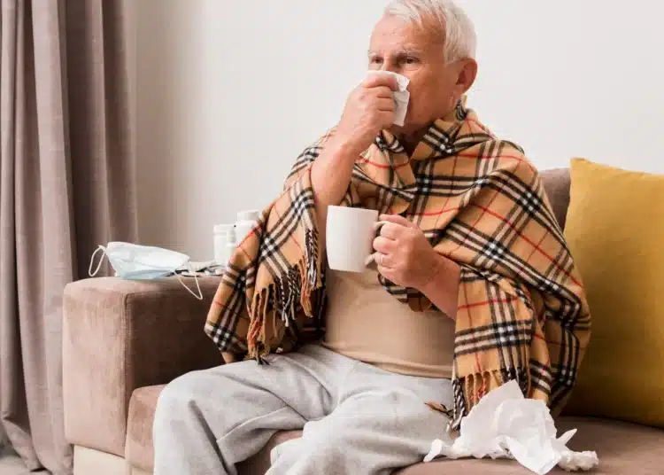 Idoso agasalhado com lenço e caneca apresenta sintomas respiratórios durante o frio.