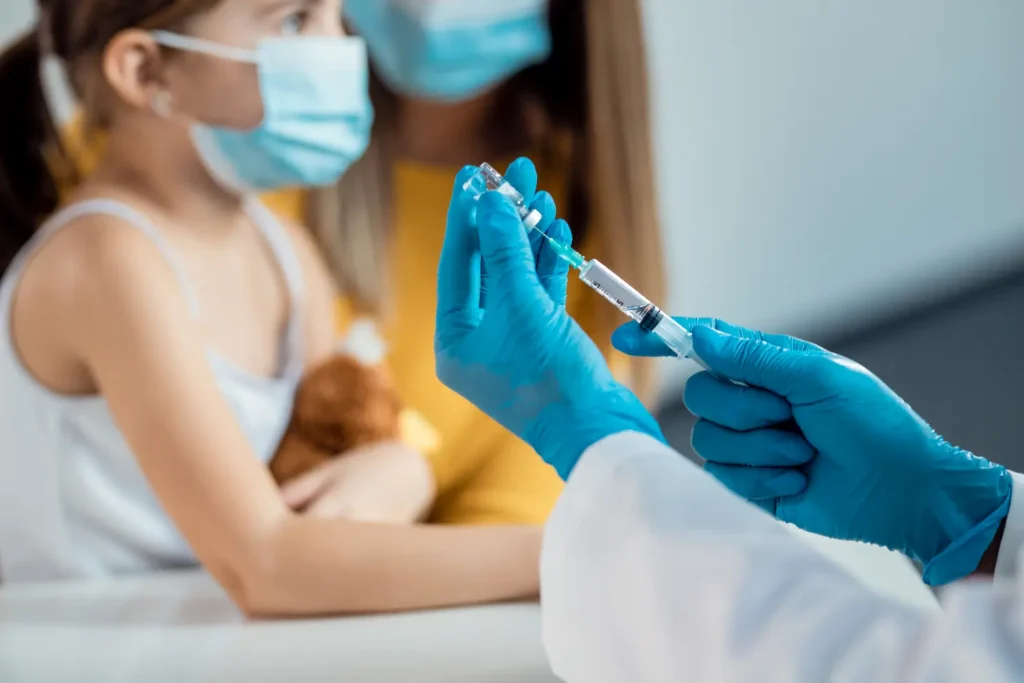 rofissional de saúde prepara uma vacina diante de uma criança acompanhada pela mãe.