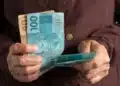 Pessoa segurando cédulas de real enquanto representa o recebimento de benefícios do INSS acima do salário mínimo.