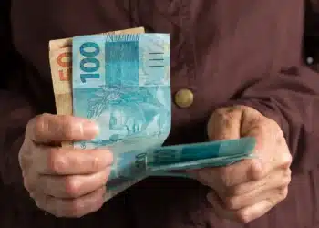 Pessoa segurando cédulas de real enquanto representa o recebimento de benefícios do INSS acima do salário mínimo.