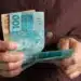 Pessoa segurando cédulas de real enquanto representa o recebimento de benefícios do INSS acima do salário mínimo.