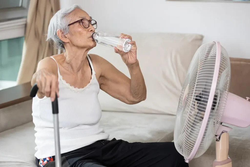 Idosa bebe água em frente a ventilador durante período de calor intenso.