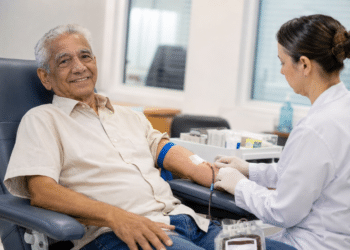 Idoso realiza doação de sangue com acompanhamento de profissional de saúde em hemocentro.