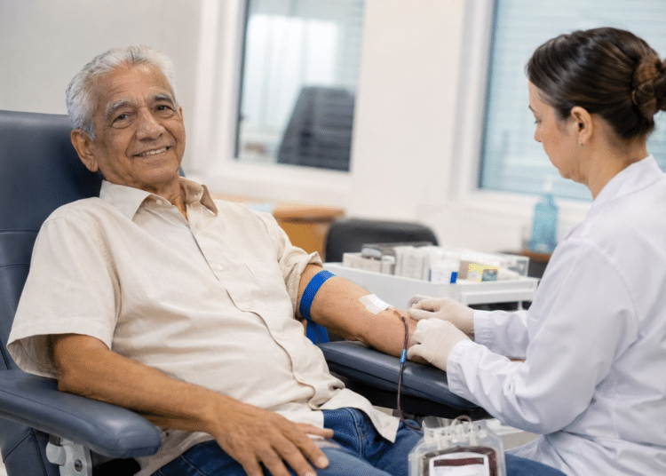 Idoso realiza doação de sangue com acompanhamento de profissional de saúde em hemocentro.