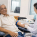 Idoso realiza doação de sangue com acompanhamento de profissional de saúde em hemocentro.