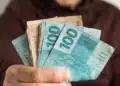 Mão segurando notas de real para representar o pagamento de aposentadorias e benefícios do INSS em agosto de 2026.