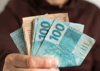 Mão segurando notas de real para representar o pagamento de aposentadorias e benefícios do INSS em agosto de 2026.