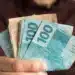 Mão segurando notas de real para representar o pagamento de aposentadorias e benefícios do INSS em agosto de 2026.