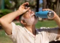 Idoso bebe água ao ar livre durante período de calor intenso.