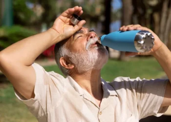 Idoso bebe água ao ar livre durante período de calor intenso.