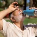 Idoso bebe água ao ar livre durante período de calor intenso.